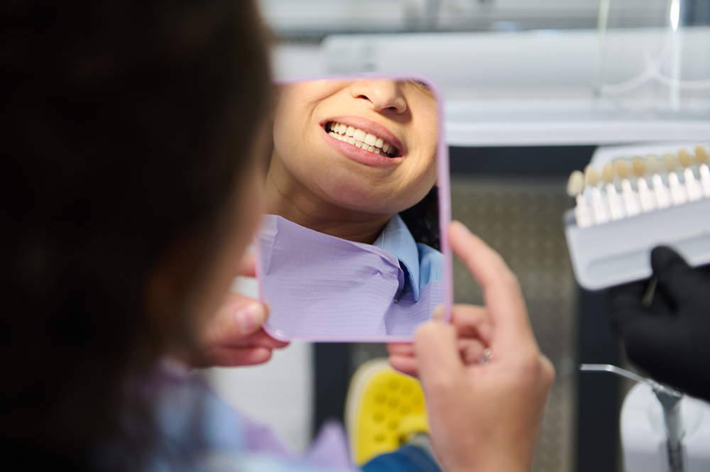 Woman looking at her teeth in a small mirror, showing the importance of maxillofacial prosthodontics 
