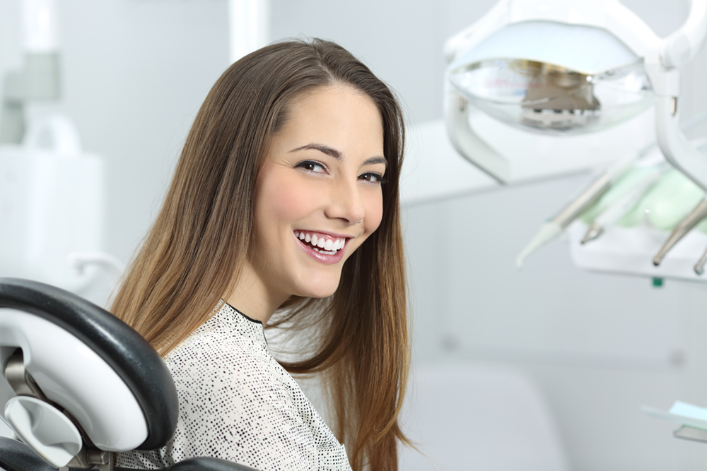 Woman in a dental chair smiling at her aesthetic smile design appointment